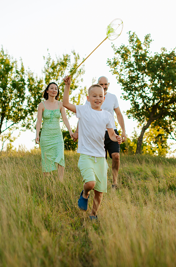 A young child running in a field with a mother and father behind him