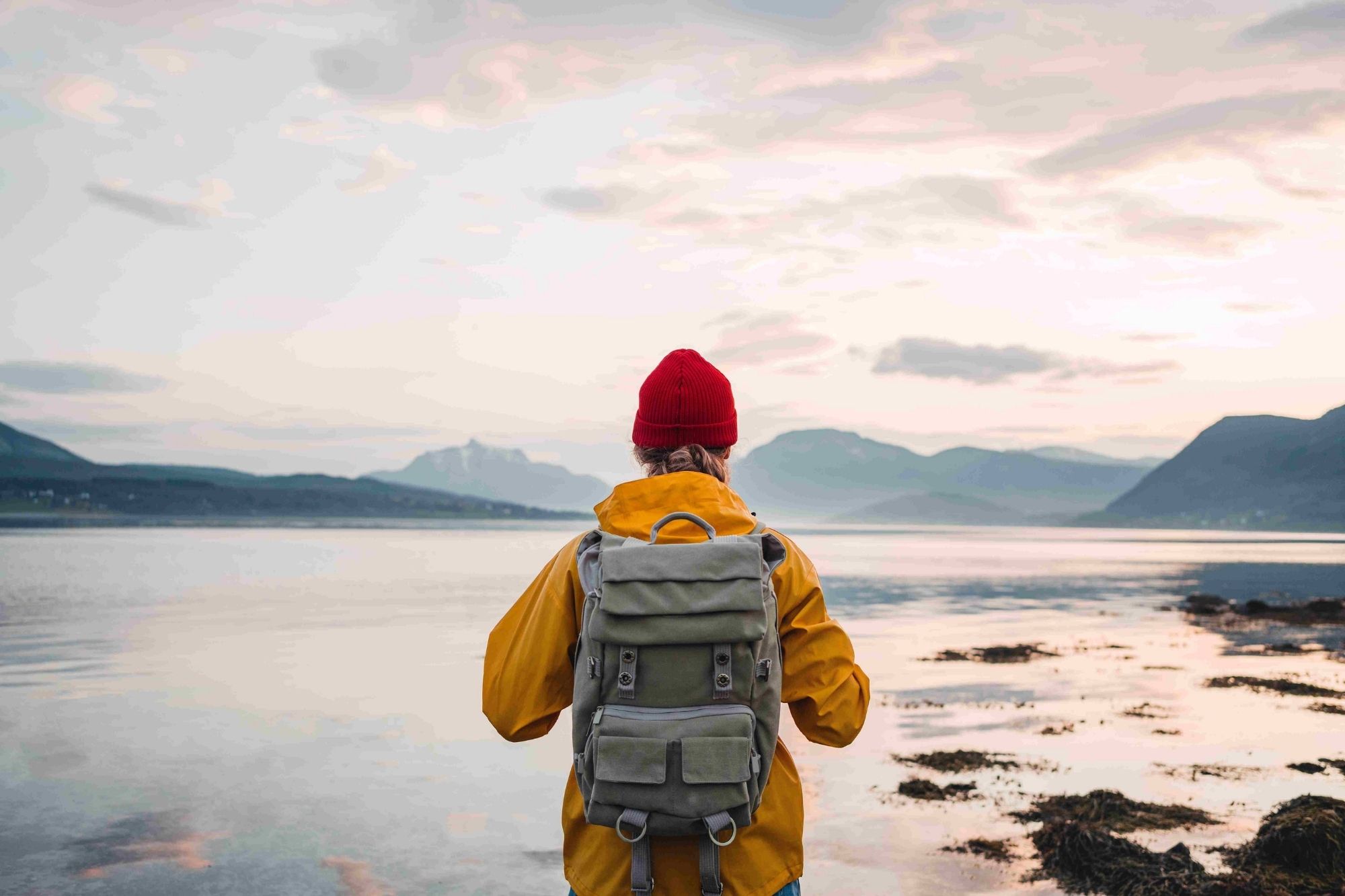 person with their back to the camera standing in front of lake with raincoat and backpack on